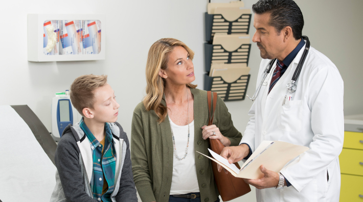  Mother and pre-teen son speaking with a doctor in exam room 