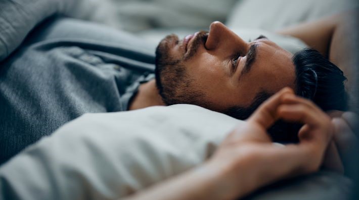 sleep deprived woman lies awake in bed and checks her alarm clock