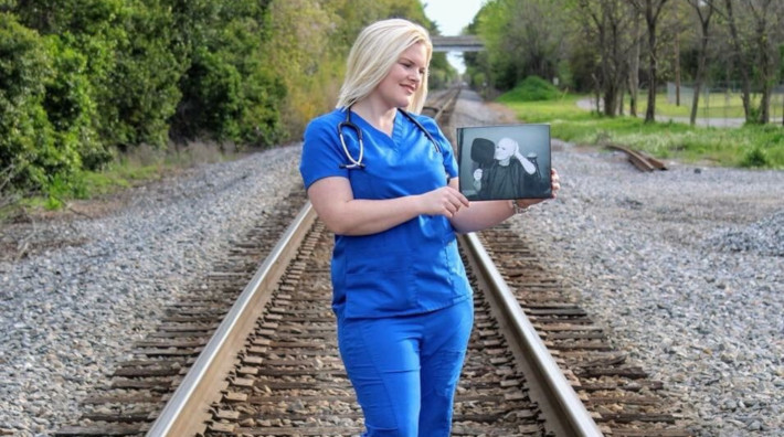 cancer survivor, Crystal Zunino, standing on a rail road track holding a picture of herself during treatment