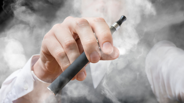 closeo up of e-cigarette in man's hand with smoke all around