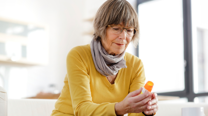 woman sitting on couch looking at the label on her prescription bottle