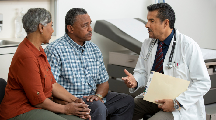 mature couple speaking with doctor in exam room