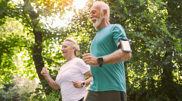 Smiling senior couple walking outside for exercise and using a pedometer to count their steps