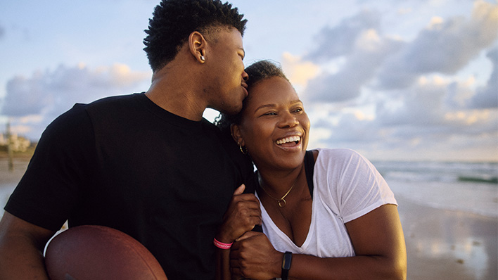 Couple smiling together on a beach, with one holding a football.