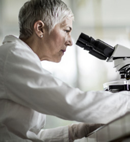 Photo of a middle aged female scientist looking into a microscope.