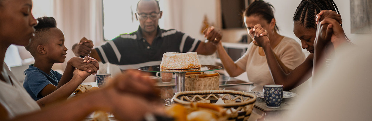 large black family holding hands while praying over food at dining table