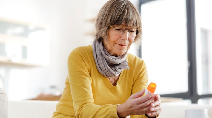 woman sitting on couch looking at the label on her prescription bottle