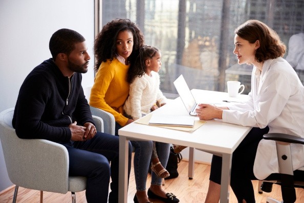 Black Parents with Daughter Across Desk from Doctor