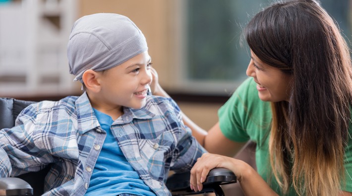 young male child cancer patient in wheelchair smiles at his mother