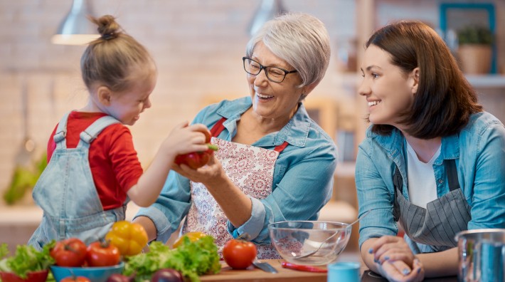Grandmother, mother and young daughter preparing fresh vegetables in kitchen