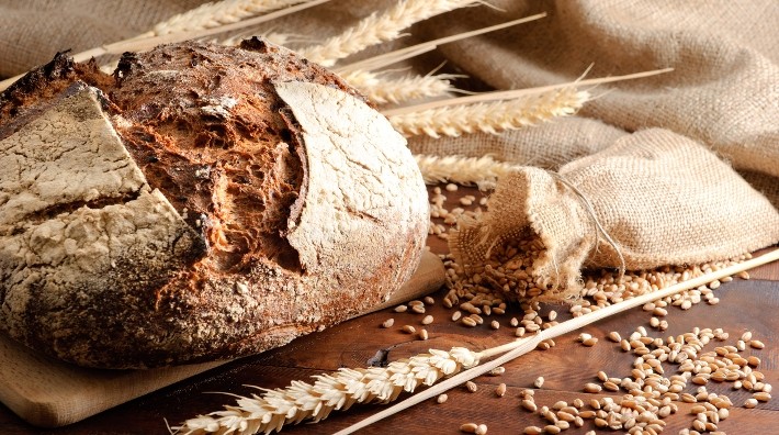 loaf of crusty bread on table surrounded by stalks of wheat
