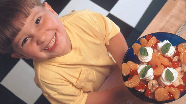 little boy smiles in front of a bowl of 30 Second Fruit Salad from the Kids’ First Cookbook