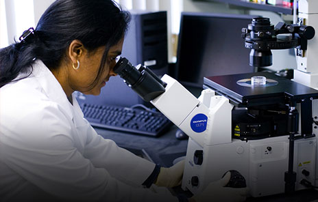 female researcher in goggles looking into a microscope in lab