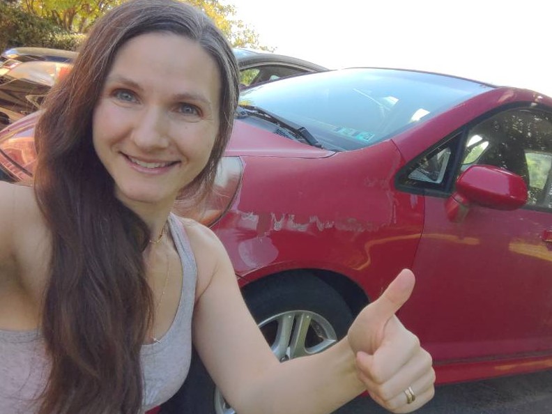 white woman with long hair kneeling in front of red car