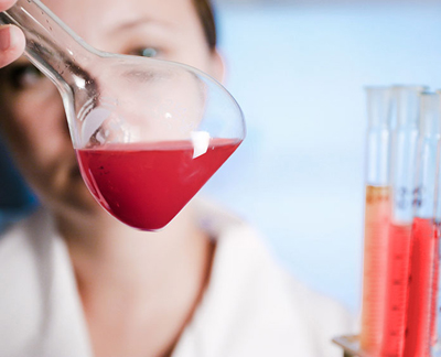 female chemist looking at red mixture in a glass flask