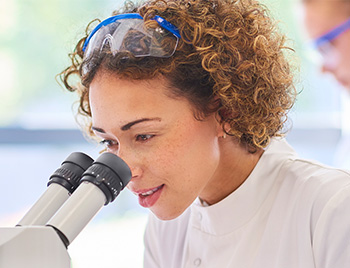 Young female doctor looking into microscope in a lab.