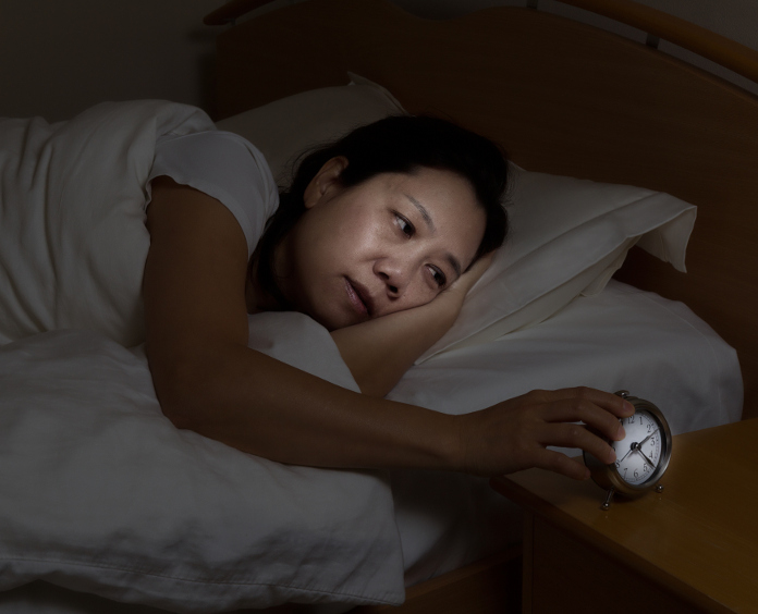 sleep deprived woman lies awake in bed and checks her alarm clock
