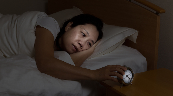 sleep deprived woman lies awake in bed and checks her alarm clock