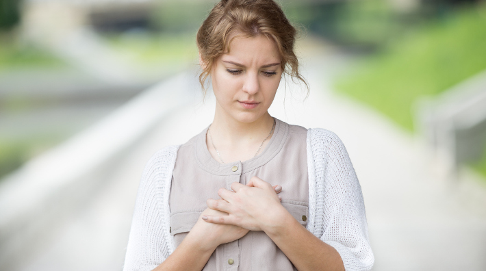 worried woman places hands on chest as if in pain