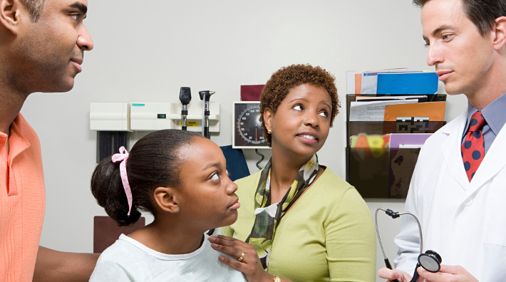 parents and their little girl talk to her doctor in an exam room