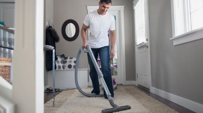 a young man vacuuming carpet in his home
