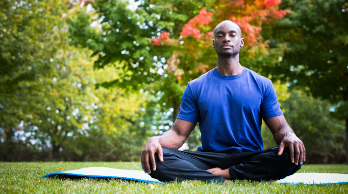 young black man wearing athletic wear sitting in the park meditating