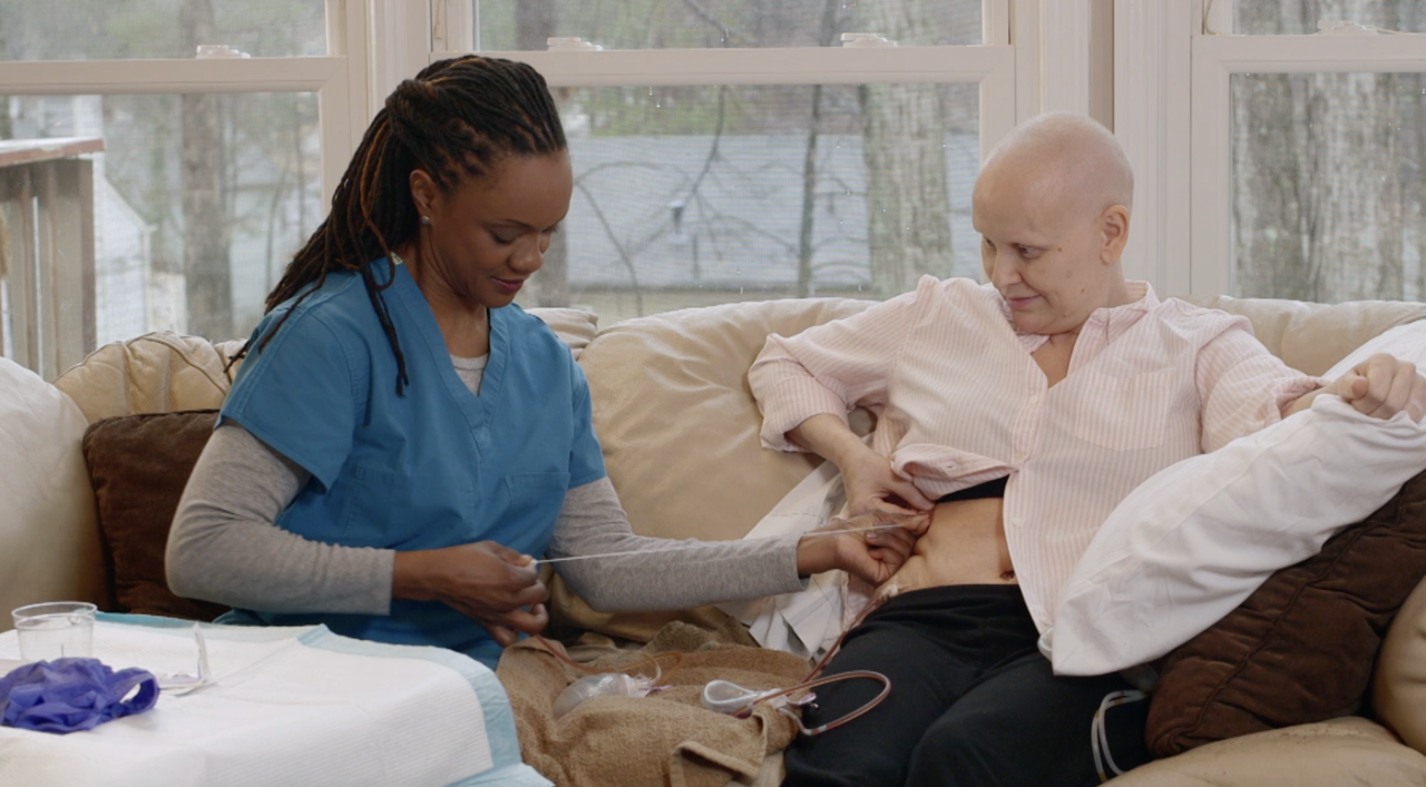 Imagen estática del video mostrando un acercamiento de una mujer siendo ayudada por una persona a cargo de su cuidado para la atención del drenaje post-quirúrgico