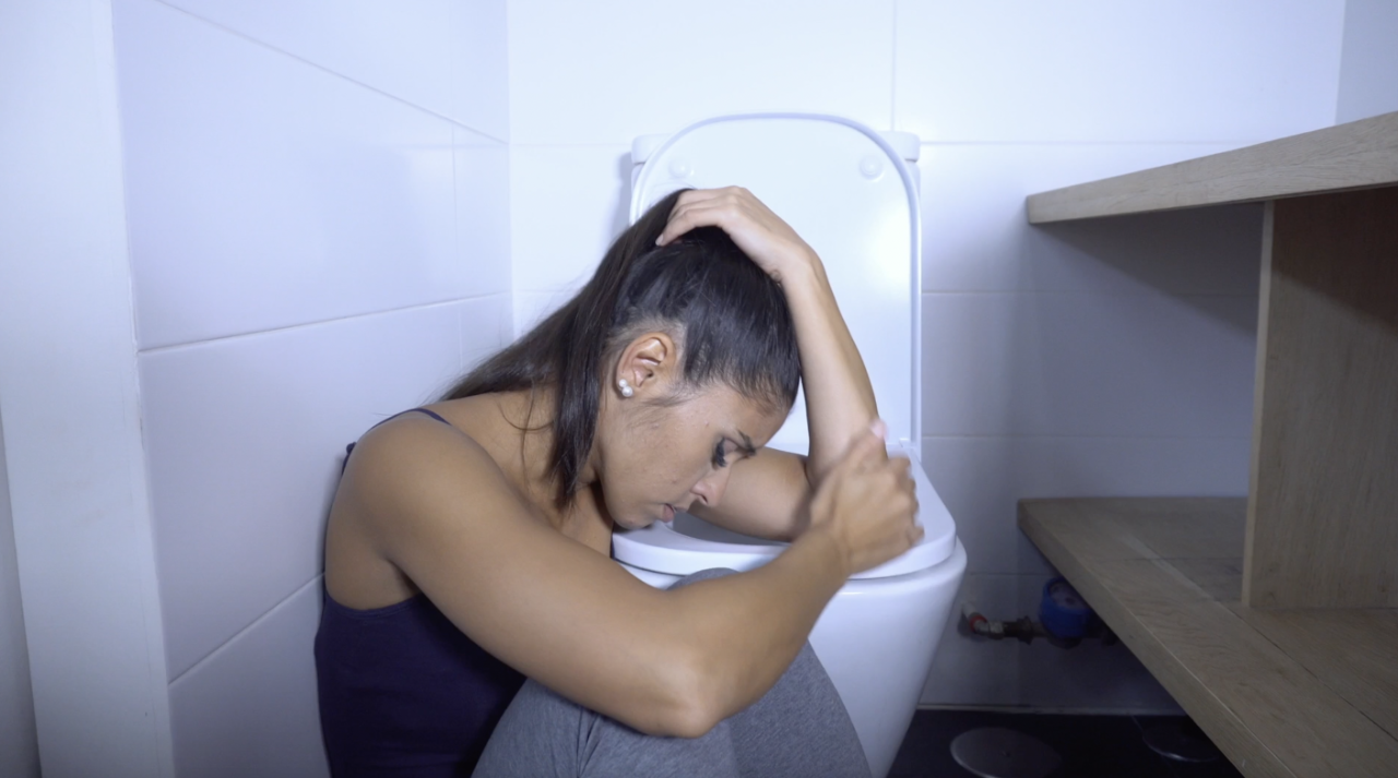 Imagen estática del video mostrando un acercamiento de  una mujer recuperándose en el suelo frente al inodoro.