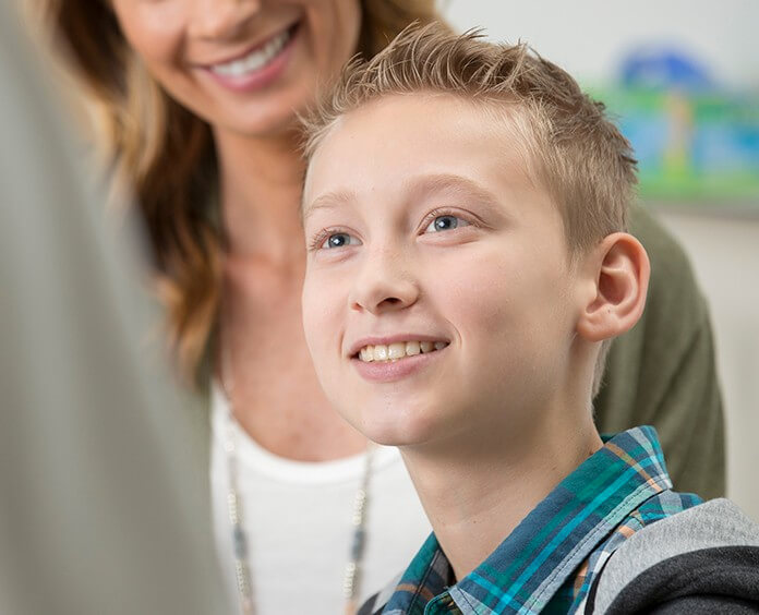 Caucasian, young male smiling at the doctor while mother stands behind him