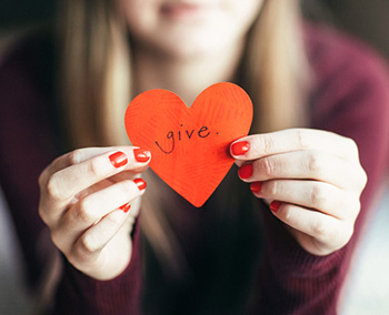 Young teen girl holding heart shaped paper cutout with the word "give" written on it.