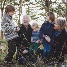 Photo of older family members laughing with their young children in a wooded area.