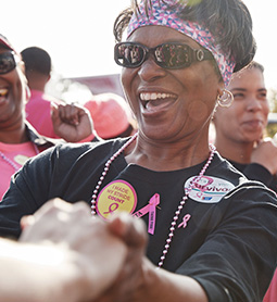 A happy smiling African American woman holding hands at an outdoor breast cancer event.
