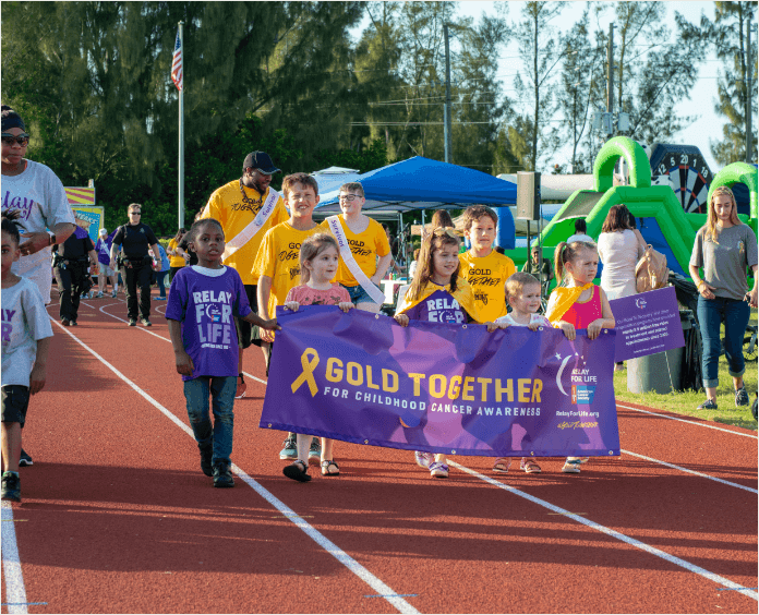 group of children holding Gold Together banner while walking on track
