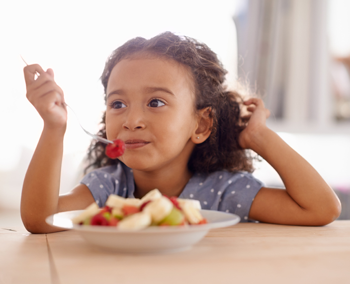 young girl sitting at table eating fruit