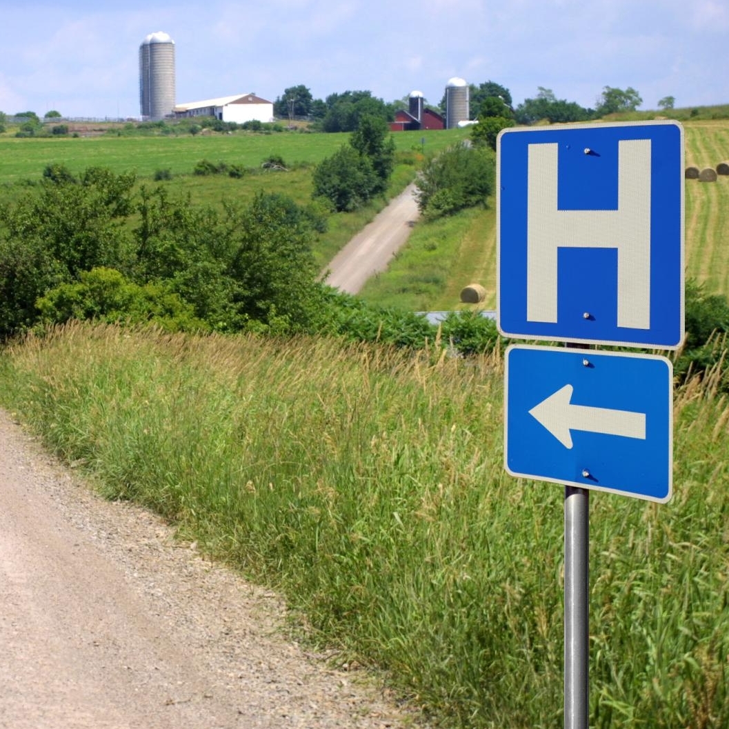 Scene with dirt road and H hospital sign with silos in background