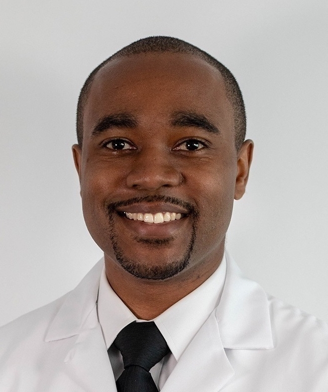 Young black man, thin beard and moustache, wearing lab coat, white shirt and black tie
