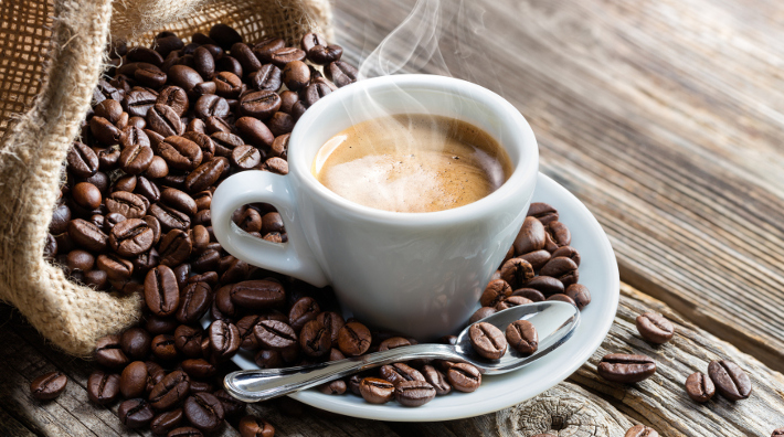 cup of hot espresso on table with a burlap sack of coffee beans