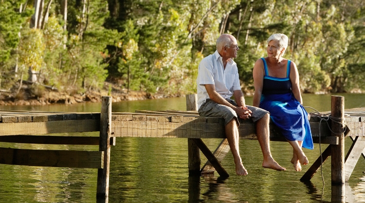 baby boomer couple sit on dock at lake