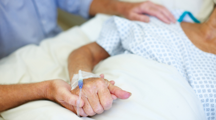 Closeup shot of an elderly man holding his wife's hand while she is ill in the hospital