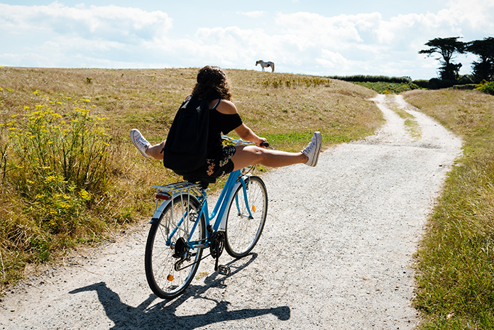 Girl on bike with feet stretched out on dirt lane facing away