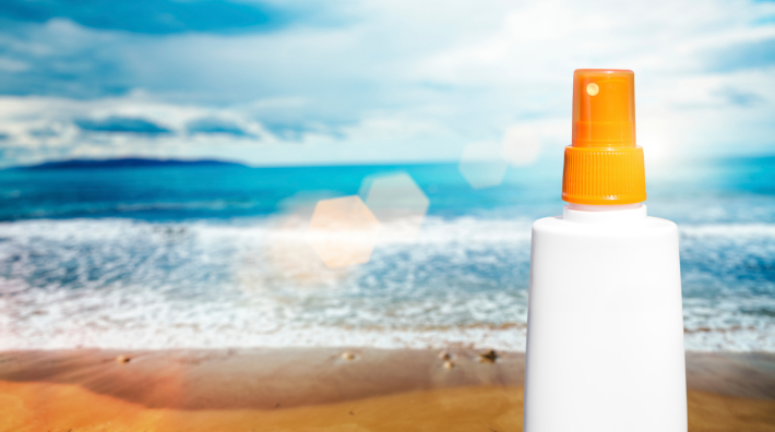 a bottle of sunscreen sits on a sandy beach with ocean in background