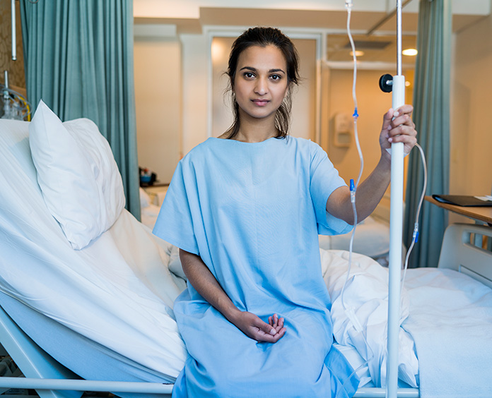 young dark skinned woman in blue gown seated on raised hospital bed holding IV