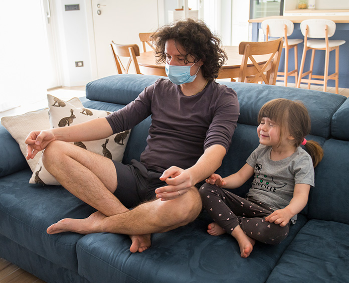 young masked man in mediating position with crossed legs seated next to toddler girl with pony tail in same position 