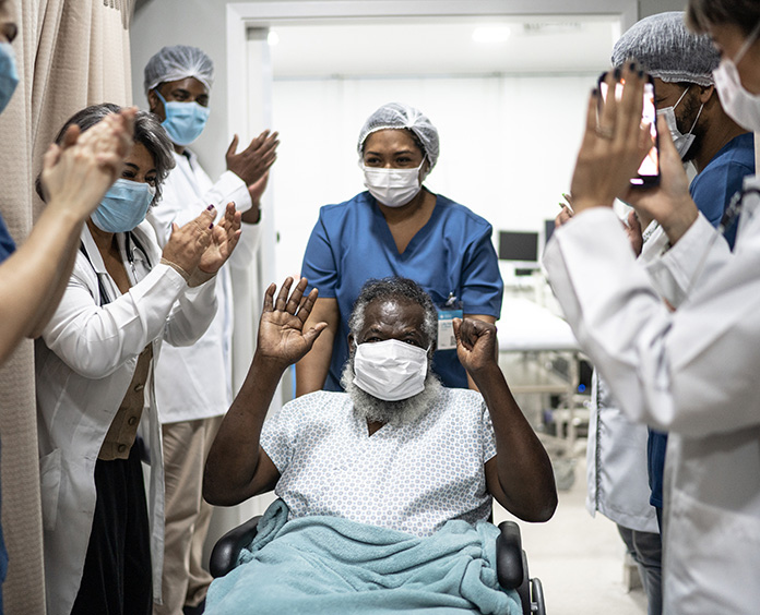 gray beard showing under mask of black man in wheel chair with hands raised cheered on by people around him