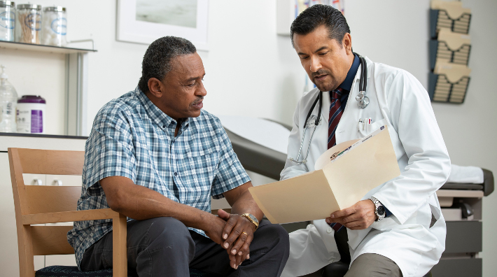 doctor goes over a chart with a male patient in exam room