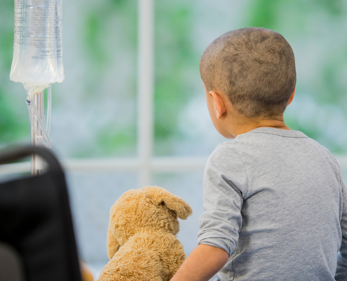 little boy with stuffed animal sits on hospital bed and gets chemotherapy