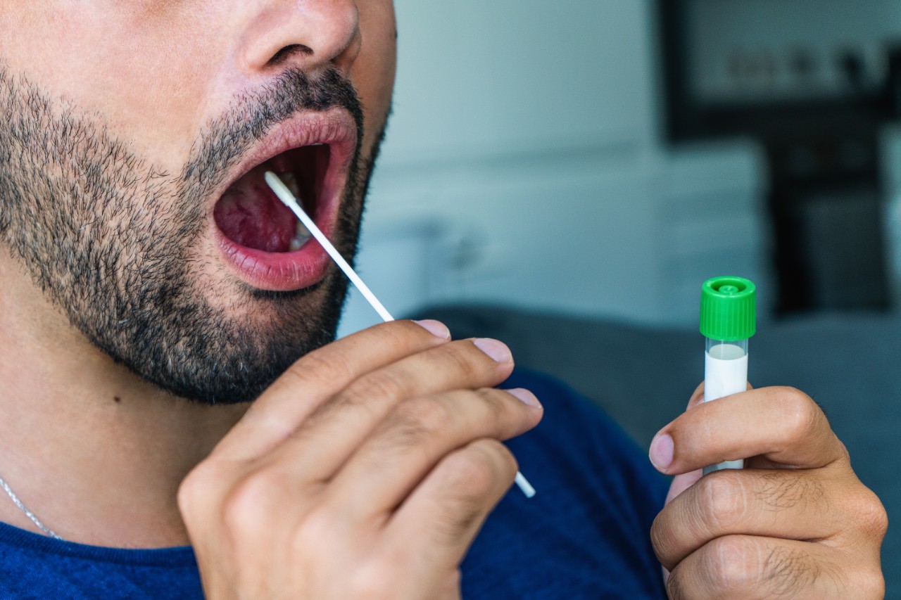 Young man  holds a swab into his mouth and a medical tube for the coronavirus / covid19 home test